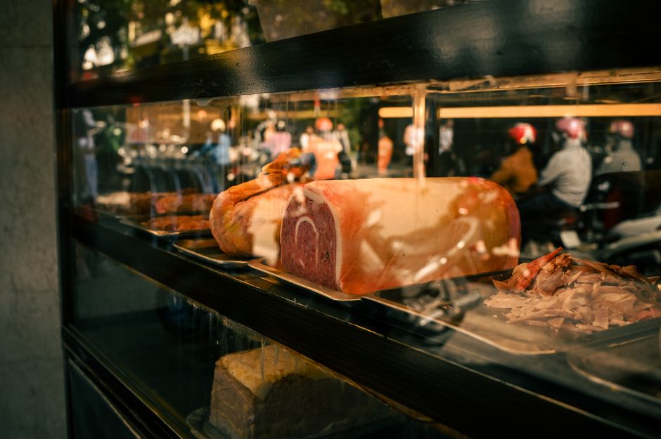 Captivating view of a deli window showcasing sliced and whole cuts of meat, with street reflections.