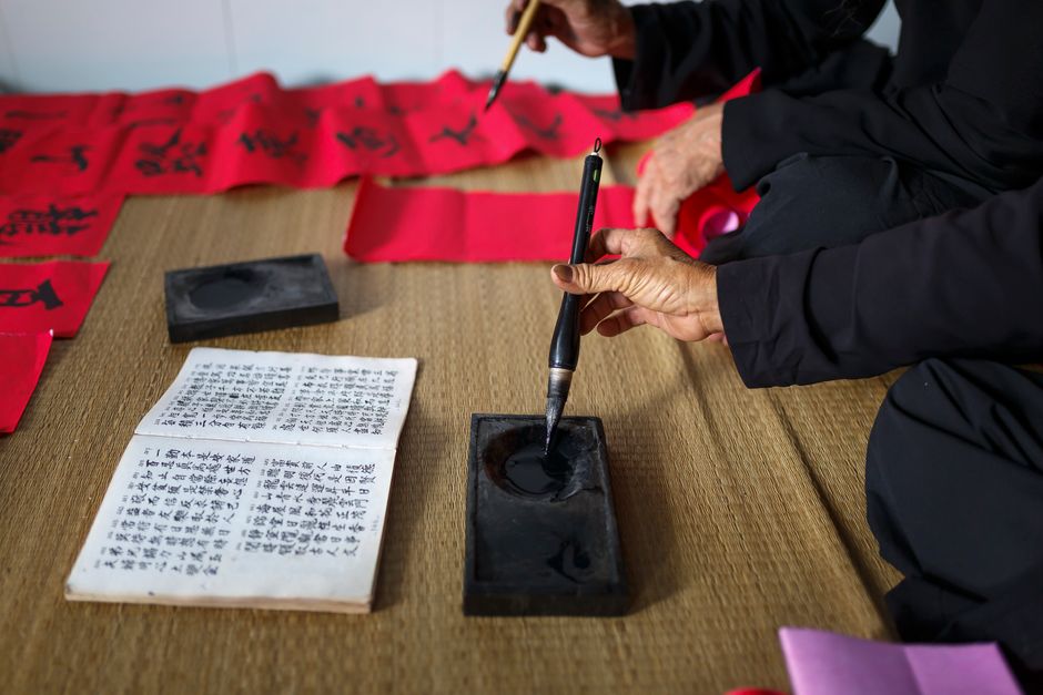 Close-up of adults practicing calligraphy on bamboo mat with ink and brush.